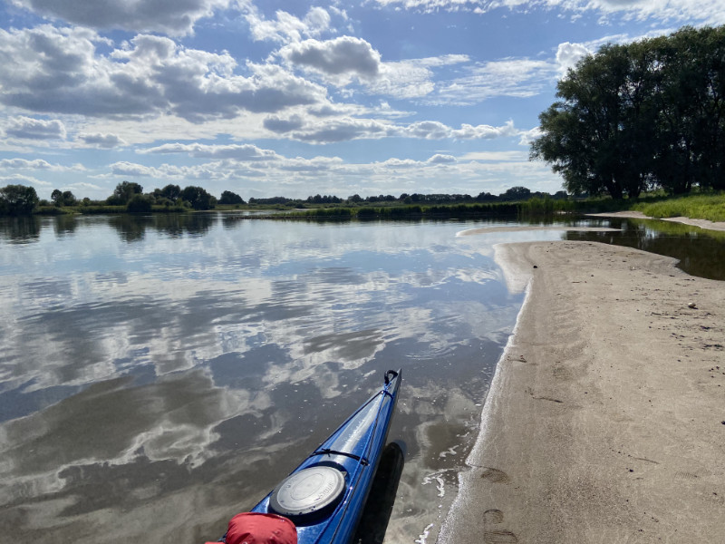 Blaues Kajak am Elbstrand, blauer Himmel, Wolken spiegeln sich im Wasser<br />
